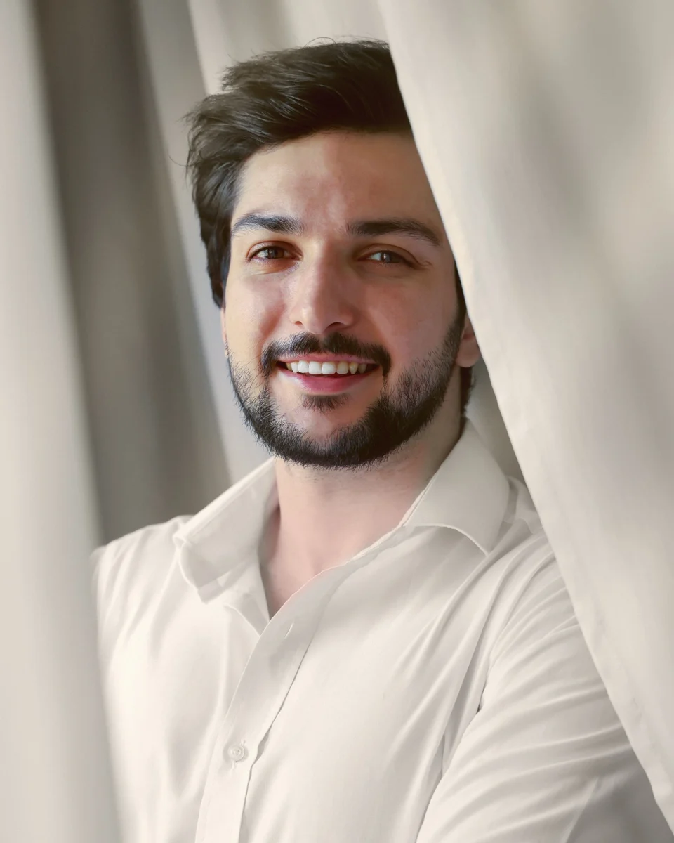 Portrait of Arch. Yazan Ghajar, smiling, in a white shirt beside a linen curtain